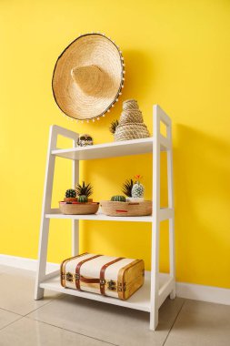 Süslü insan kafatasına sahip beyaz raf ünitesi ve sarı duvarda asılı sombrero.