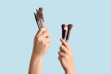 Mavi arka planda makyaj fırçası olan kadın elleri