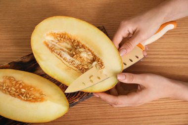 Kahverengi ahşap arka planda taze kavun kesen kadın.