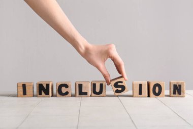 Beyaz döşeme masasındaki tahta küplerden kadın eli INCLUSION yapıyor