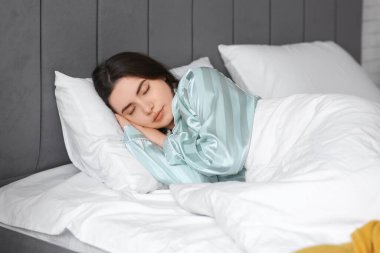 Güzel genç bir kadın rahat bir yatakta uyuyor.