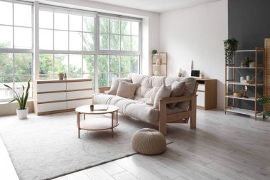 Oturma odasının içinde bej kanepe, masa ve büyük pencere var.