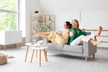 Elinde oje örnekleri olan genç kadınlar oturma odasında pedikür yapıyor.