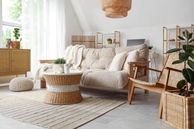 Oturma odasının iç tarafında rahat bir kanepe ve ev bitkisi olan bir hasır masa.