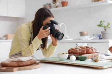 Profesyonel fotoğraf makinesi olan genç bir kadın fotoğrafçı modern mutfakta yemek fotoğrafı çekiyor.
