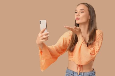 Cep telefonlu genç bir kadın bej arka planda selfie çekiyor.