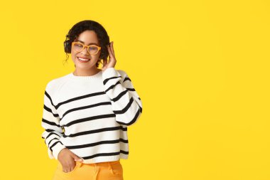 Sonbahar kıyafetleri ve sarı arka planda kulaklıkları olan güzel, mutlu, Afro-Amerikan bir kadın.