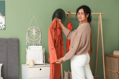 Güzel, genç, mutlu, Afro-Amerikan kadın evde sonbahar kıyafeti seçiyor.