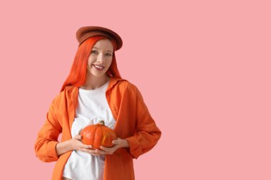 Pembe arka planda balkabağı olan bereli güzel, genç ve mutlu bir kadın.