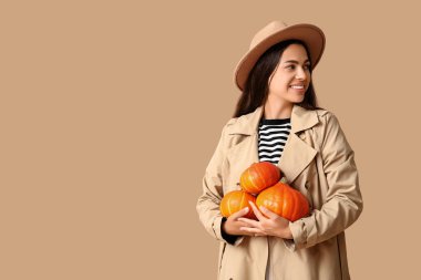 Kahverengi arka planda taze balkabakları olan zarif genç bir kadın.