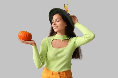 Gri arka planda taze balkabağı ve sonbahar yaprağı olan zarif genç bir kadın.