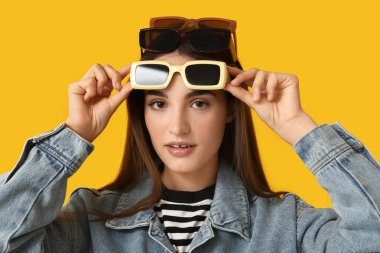 Sarı arka planda farklı stil güneş gözlüklü güzel bir genç kadın.