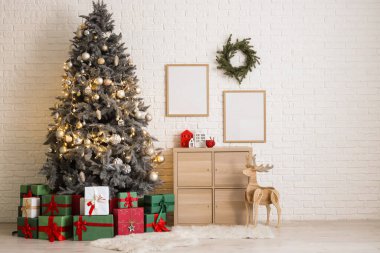 Noel ağacı hediye kutuları, şenlikli dekorasyonlar ve beyaz tuğla duvarın yanındaki ahşap dolap.