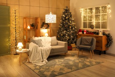 Oturma odasının içinde kanepe, Noel ağacı ve geceleri parlayan lambalar.