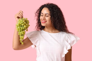 Pembe arka planda olgun üzümleri olan mutlu Afro-Amerikalı bir kadın.