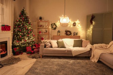 Şenlikli oturma odasının içinde şömine, Noel ağacı ve akşamları parlayan ışıklar.