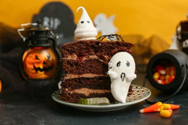 Bir parça tatlı Cadılar Bayramı pastası. İçinde hayaletler ve siyah masanın üstünde sarı arka planda mısır şekeri var.