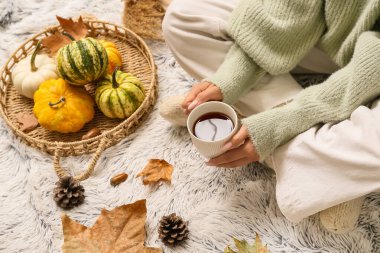 Sonbahar yaprakları, balkabakları ve arka plan olarak beyaz ekoseli bir fincan çay ile sıcak çoraplar içindeki kadın bacakları.