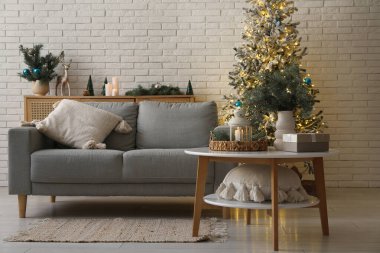 Oturma odasının içinde kanepe, masa ve parıldayan Noel ağacı var.