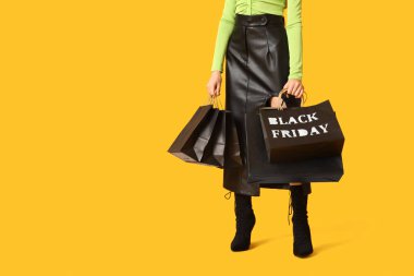 Sarı arka planda alışveriş torbaları olan şık genç bir kadın. Kara Cuma İndirimi