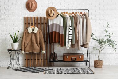 Beyaz tuğlalı duvarın yanında şık süveterler var.