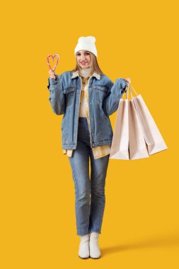 Sarı arka planda şeker kamışları ve alışveriş torbalarıyla güzel genç bir kadın.