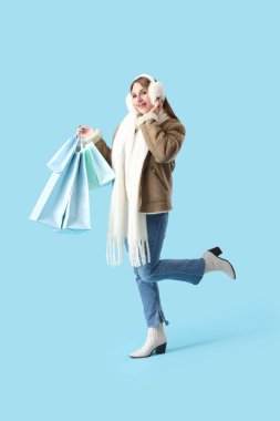 Mavi arka planda alışveriş torbaları olan güzel genç bir kadın.
