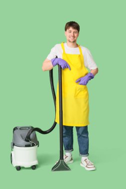 Yeşil arka planda modern elektrik süpürgesi olan genç bir erkek hademe.