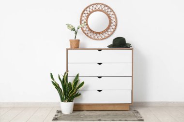 Odanın ışık duvarında keçeli şapkalı, çiçekli ve aynalı çekmeceler.