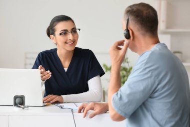 Kadın doktor klinikte hastanın işitmesini kontrol ediyor.