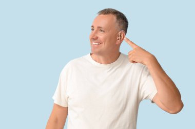 Mavi arka planda işitme cihazına işaret eden olgun bir adam