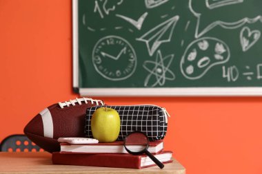Elma, büyüteç, rugby topu ve kitaplı kalem kutusu sınıfta, yakın plan.