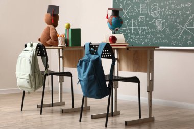 Sırt çantalı masalar, mezuniyet şapkaları ve sınıfta oyuncaklar.