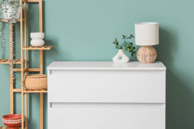 Odadaki yeşil duvarın yanında klozette bitki dalları olan lamba ve vazo.