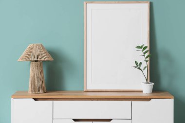 Boş çerçeveli lamba ve yeşil duvarın yanındaki çekmecelerin üzerine yerleştirilmiş.