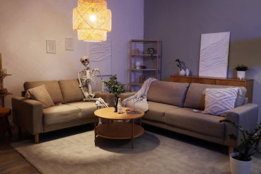 Geceleri oturma odasındaki koltukta oturan insan iskelet modeli.