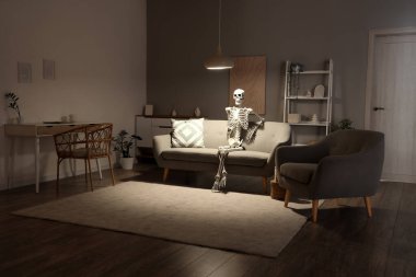 Geceleri oturma odasındaki gri koltukta oturan insan iskelet modeli.