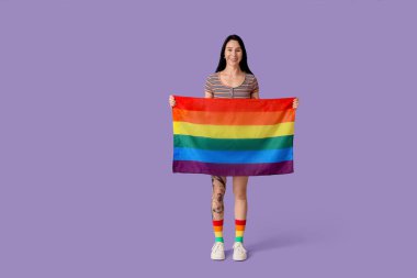 Leylak arka planında LGBT bayrağı olan dövmeli genç bir kadın.