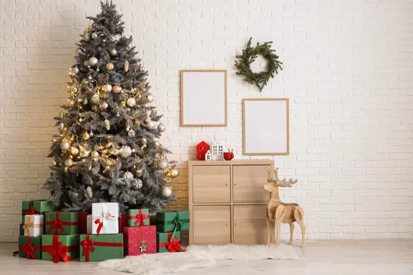 Noel ağacı hediye kutuları, şenlikli dekorasyonlar ve beyaz tuğla duvarın yanındaki ahşap dolap.