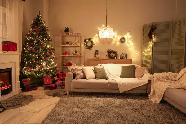 Şenlikli oturma odasının içinde şömine, Noel ağacı ve akşamları parlayan ışıklar.