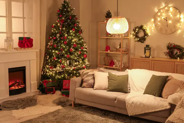 Şenlikli oturma odasının içinde şömine, Noel ağacı ve akşamları parlayan ışıklar.