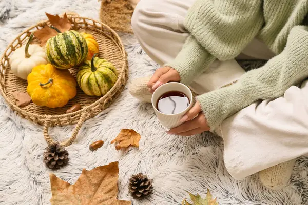 Sonbahar yaprakları, balkabakları ve arka plan olarak beyaz ekoseli bir fincan çay ile sıcak çoraplar içindeki kadın bacakları.
