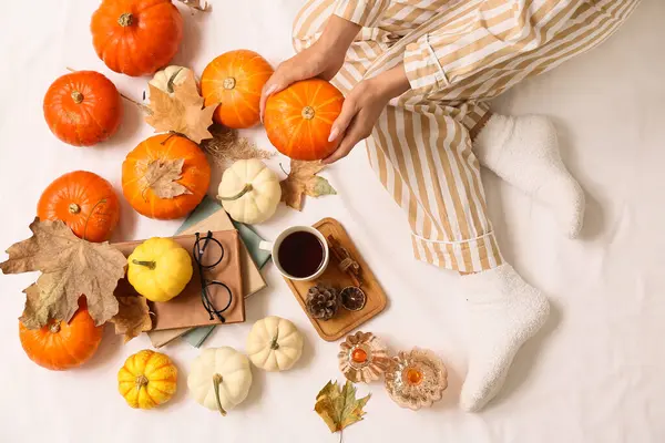 Sonbahar yaprakları, kitaplar, bir fincan kahve ve yatağın üzerinde balkabağı olan kadın çorapları.