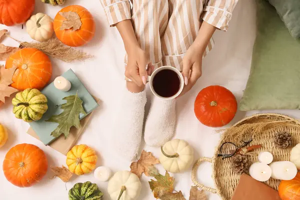 Sonbahar yapraklı, sıcak çoraplı kadın bacakları, yatakta bir fincan kahve ve balkabağı.