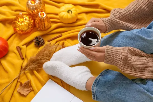 Sonbahar balkabakları, ekose ve sarı arka planda bir fincan çay ile sıcak çoraplar içindeki kadın bacakları.