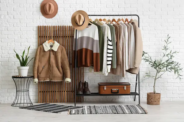 Beyaz tuğlalı duvarın yanında şık süveterler var.