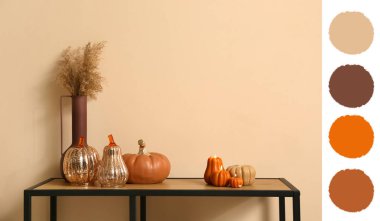 Evdeki bej duvarın yanındaki masada vazo ile balkabağı şeklinde mumlar yakıyor.