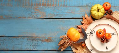 Cadılar Bayramı masası, balkabakları, sonbahar yaprakları ve mavi ahşap arka planda örümcekler.
