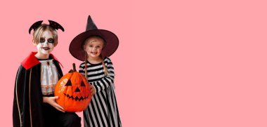 Cadılar Bayramı için giyinmiş küçük çocuklar pembe arka planda balkabağı tutarken mesaj için yer açıyorlar.