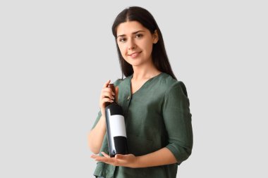 Hafif arka planda şarap şişesi olan genç bir kadın.